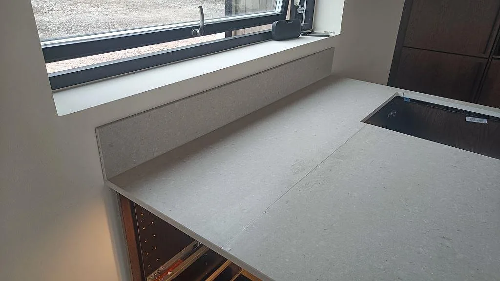 Matt Caesarstone Clamshell som köksbänkskiva med låg stenkant vid fönstret och förberett urtag i ett kök i Nättraby.