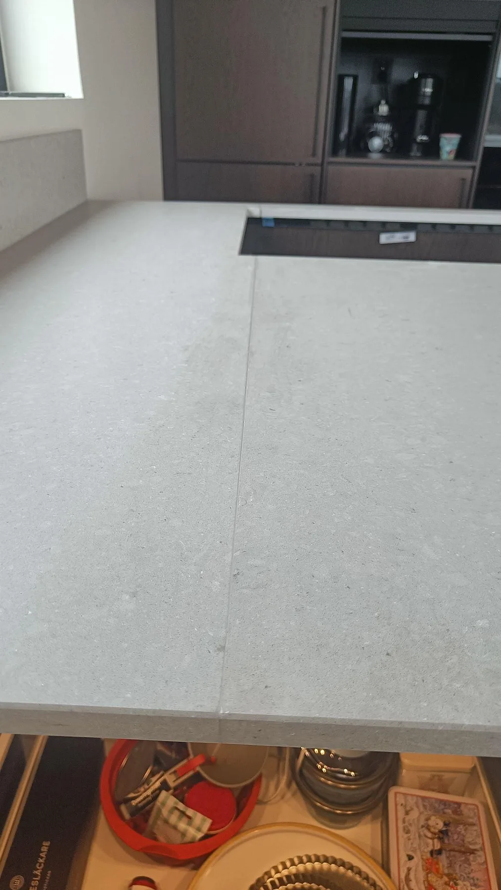 Detalj av skarv i matt Caesarstone Clamshell på en köksö med ljusgrå struktur och öppna lådor i Nättraby.