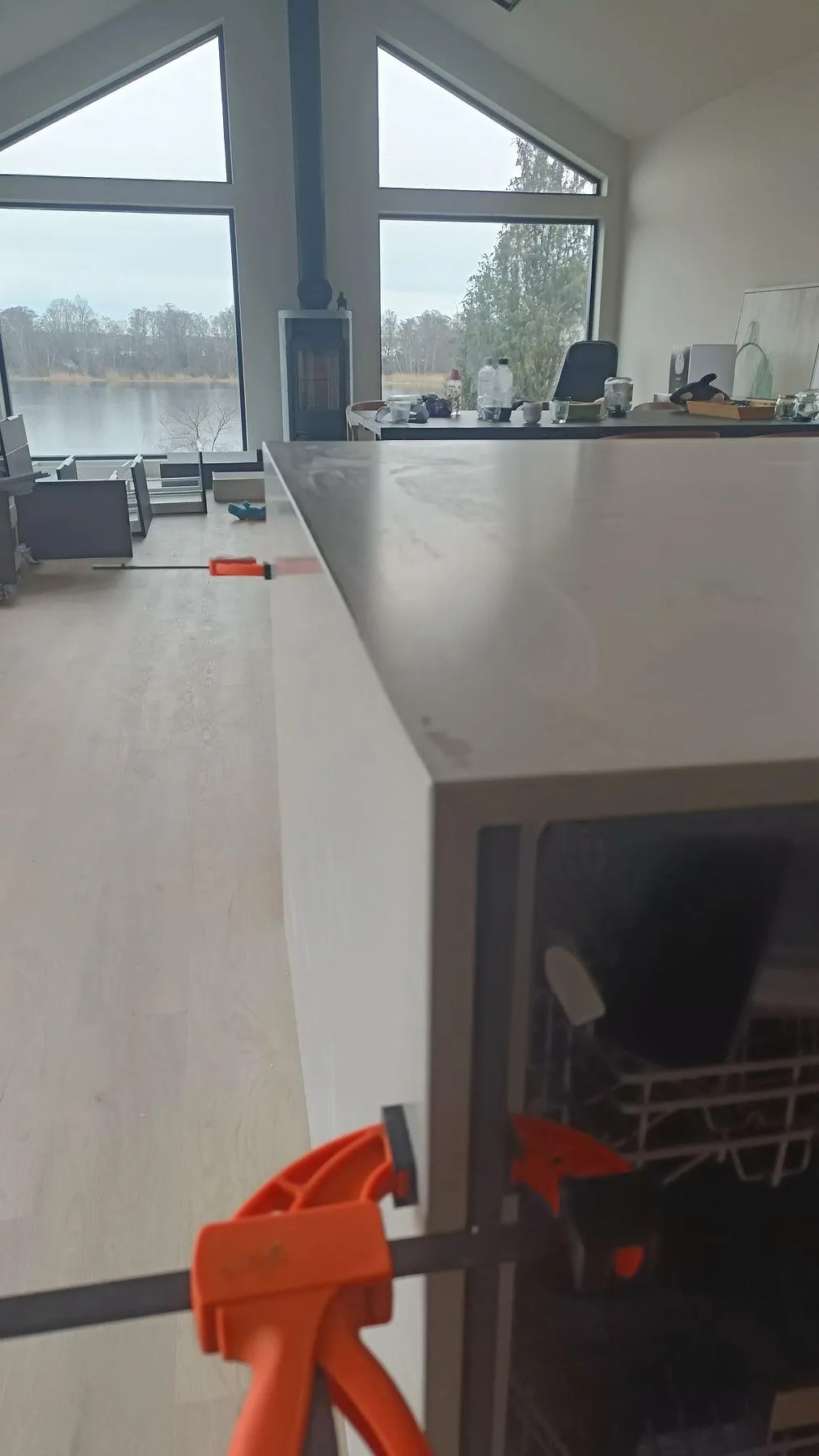 Sidovy av köksö i matt Caesarstone Clamshell med nedgående gavel, tving och stora fönster mot vattnet i Nättraby.