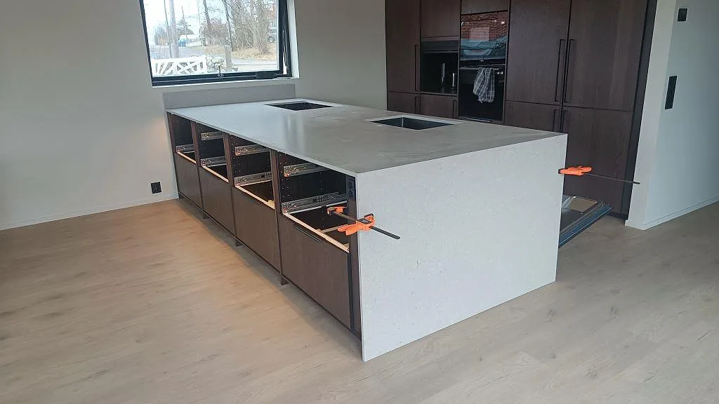 Köksö och köksbänkskiva i matt Caesarstone Clamshell, 20 mm kvartskomposit, under montering i ett kök i Nättraby.