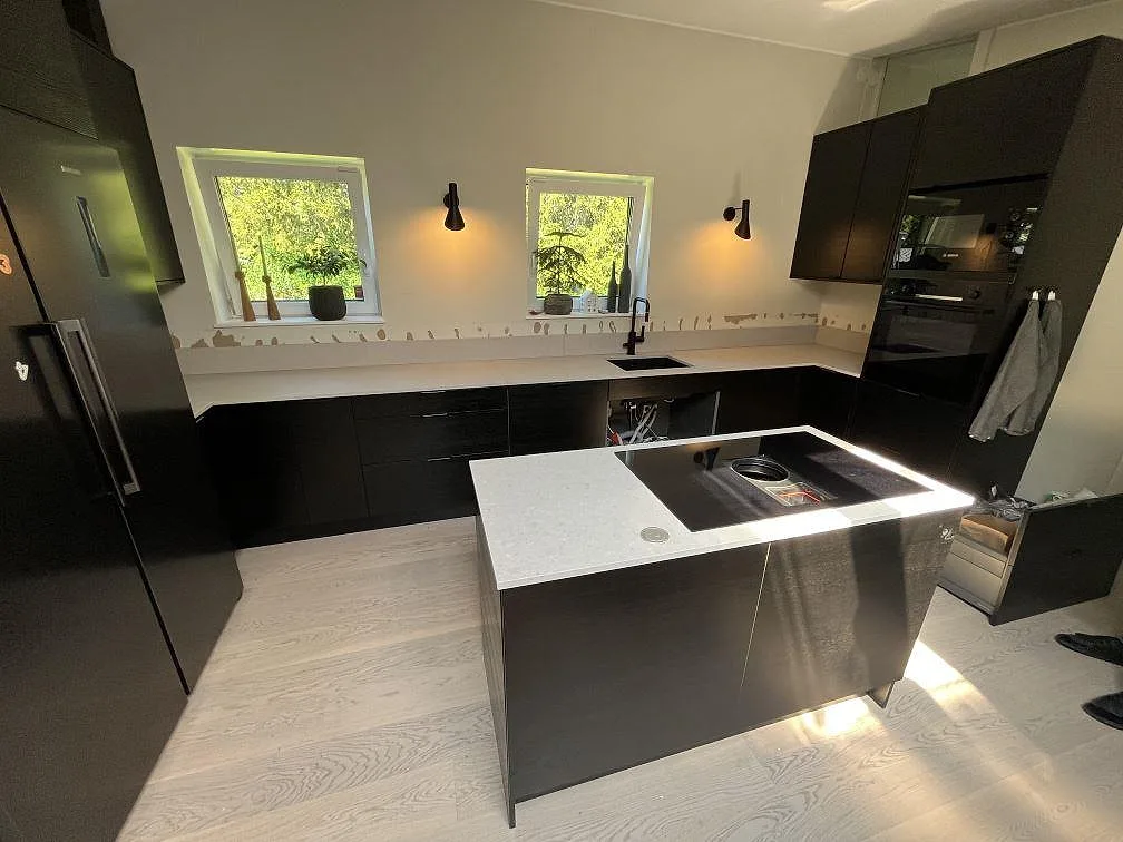 Matt Caesarstone Clamshell komposit som köksbänkskiva med köksö, mörka köksskåp och synlig diskho i Saltsjö boo.