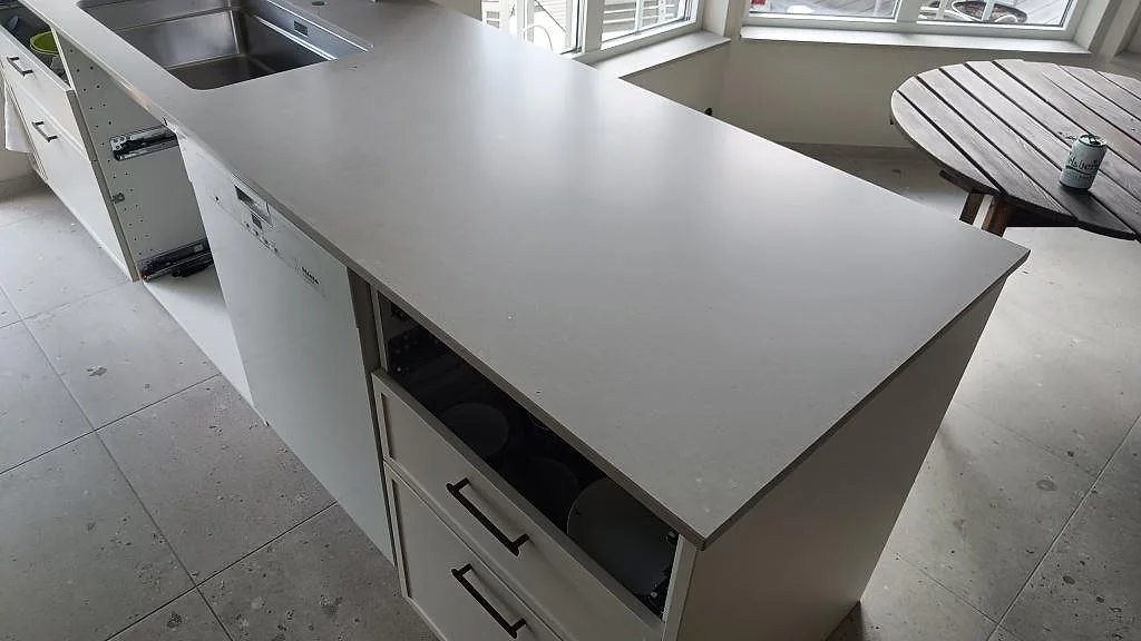 Stor köksö i matt Caesarstone Clamshell med underlimmad diskho och vita köksstommar i ett kök i Södra Sandby.