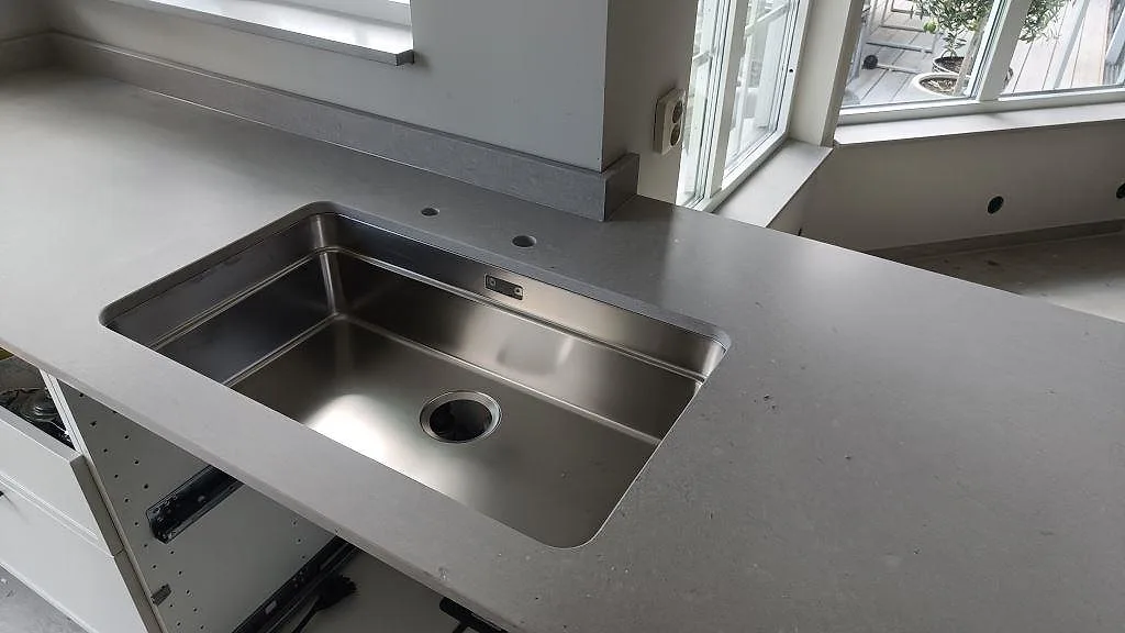 Närbild på underlimmad rostfri diskho i köksbänkskiva av matt Caesarstone Clamshell i Södra Sandby.