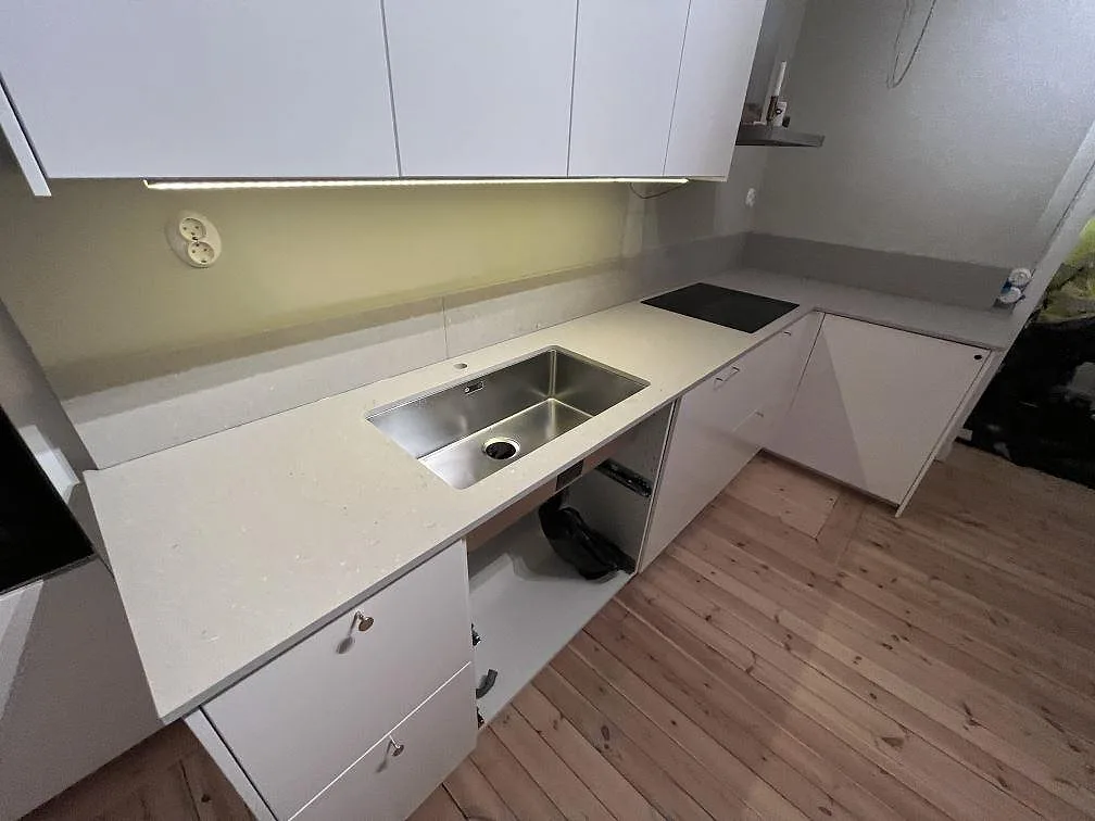 L-formad köksbänkskiva i matt Caesarstone Clamshell komposit med diskho ovanpå stenen, induktionshäll och låg stänkkant i ett kök i Solna.