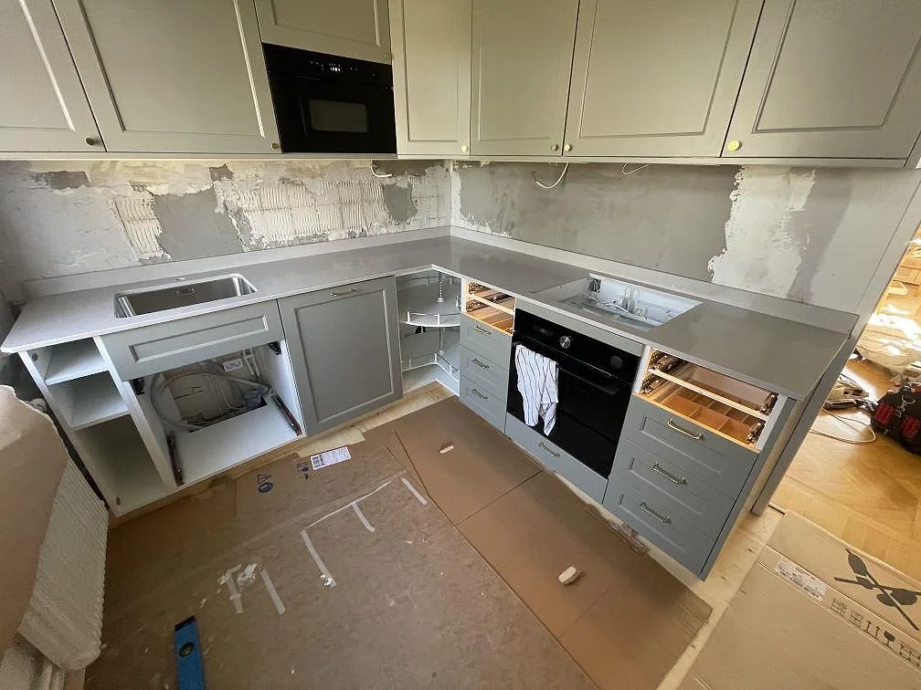 U-formad köksbänkskiva i Caesarstone Clamshell komposit, polerad, med diskho och hällzon under montering i Stockholm.