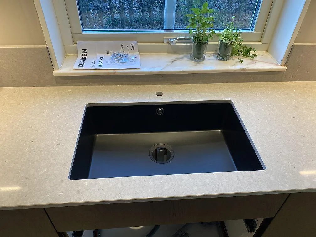 Polerad köksbänkskiva i Caesarstone Clamshell med svart diskho vid fönster och låg stänkkant i Torslanda.