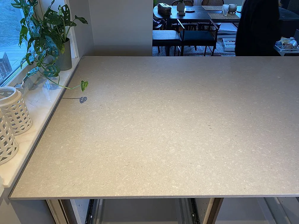 Stor köksö i ljusgrå polerad Caesarstone Clamshell komposit med öppna skåpstommar i Torslanda.