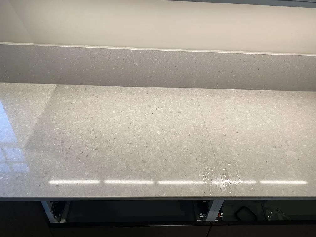 Närbild på polerad Caesarstone Clamshell bänkskiva med stänkkant och ljusreflexer i ett kök i Torslanda.