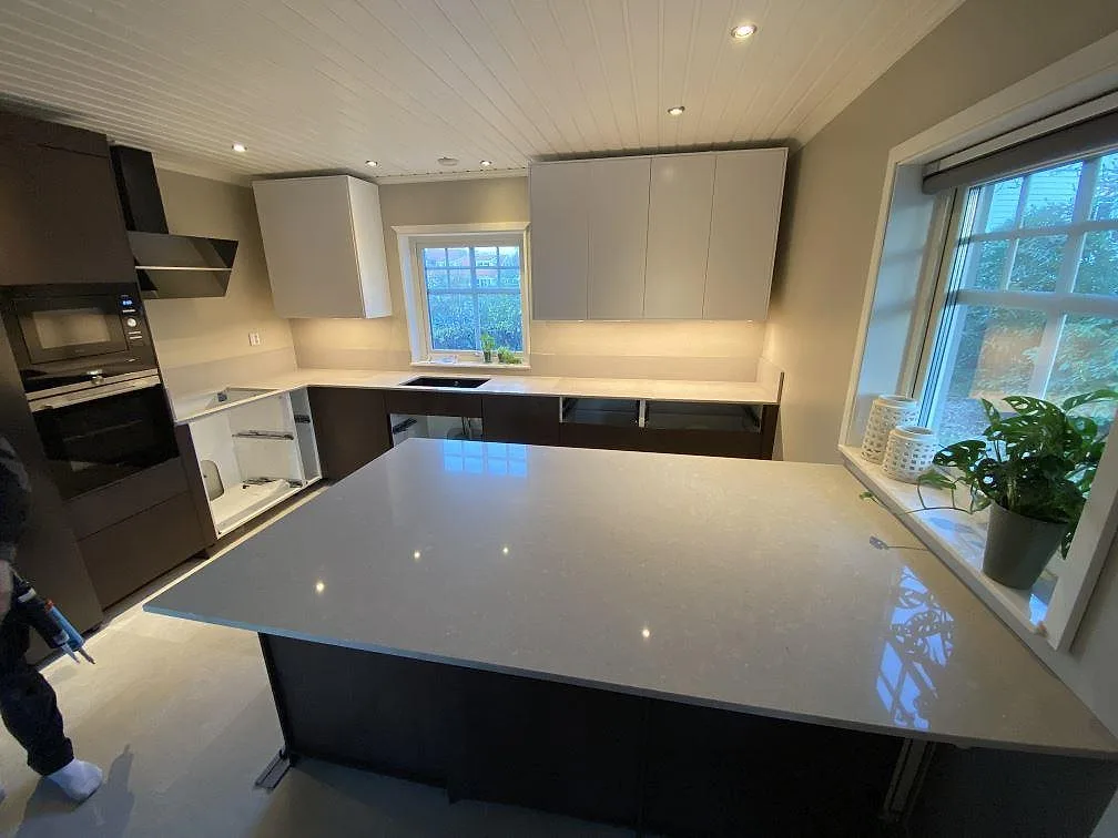 Köksbänkskiva och köksö i polerad Caesarstone Clamshell, ljusgrå komposit, under montering i ett kök i Torslanda.