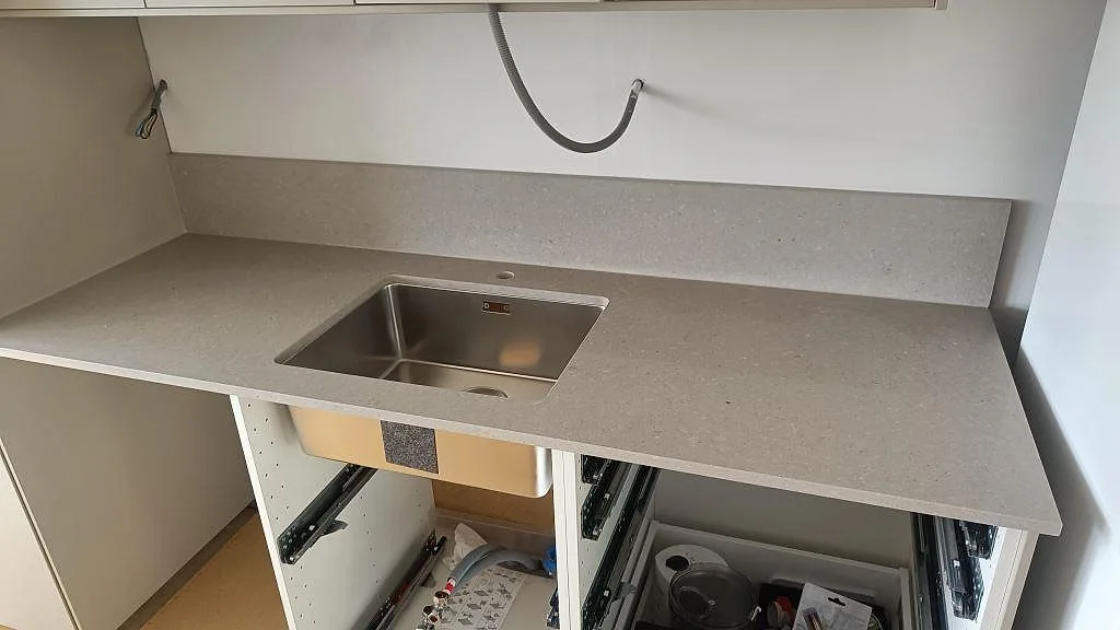 Väggmonterad köksbänkskiva i Caesarstone Clamshell, polerad kvartskomposit, med rostfri diskho och uppvikt stänkkant i Torslanda.