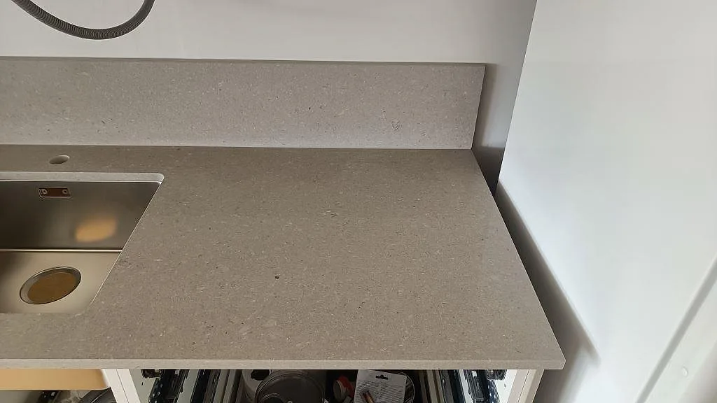 Ytdetalj av Caesarstone Clamshell, polerad ljusgrå kvartskomposit, vid rostfri diskho och stänkkant i Torslanda.