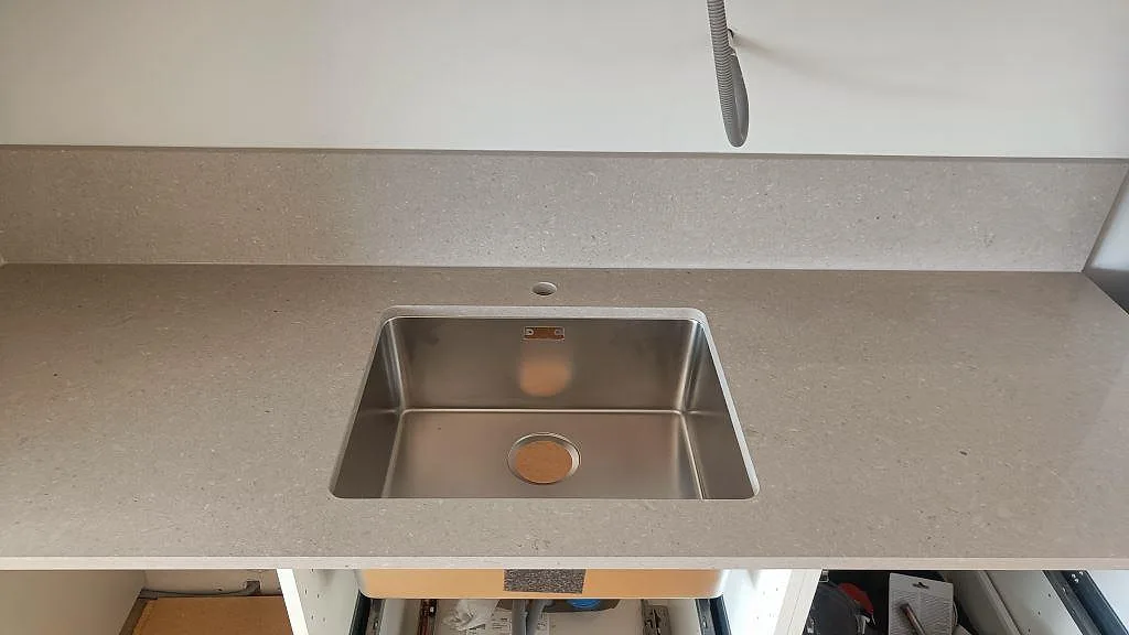Rostfri diskho underlimmad i Caesarstone Clamshell, polerad komposit, med låg stänkkant i ett kök i Torslanda.