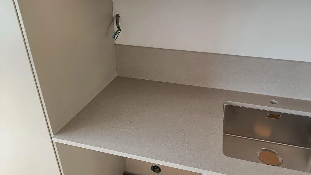 Ljusgrå köksbänkskiva i Caesarstone Clamshell, polerad komposit, med stänkkant och vit köksinredning i Torslanda.