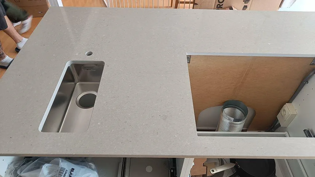 Närbild av köksö i ljusgrå Caesarstone Clamshell, polerad kvartskomposit, med rostfri diskho och urtag under montering i Torslanda.