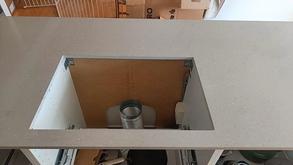 Detalj av rektangulärt urtag i köksö av Caesarstone Clamshell, polerad komposit, i ett kök under montering i Torslanda.