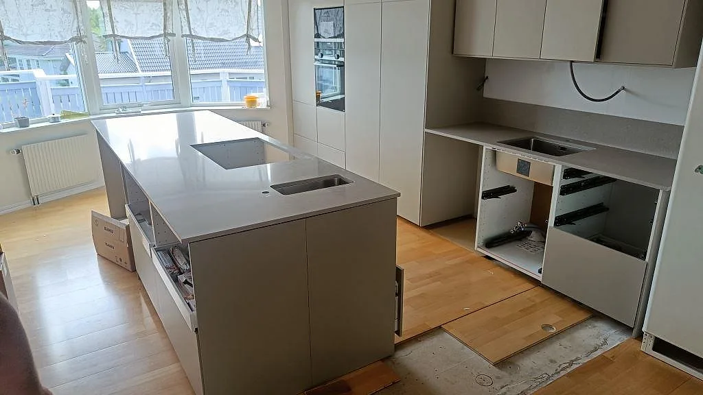 Köksbänkskiva och köksö i Caesarstone Clamshell, polerad kvartskomposit, med vit inredning och stora fönster i Torslanda.