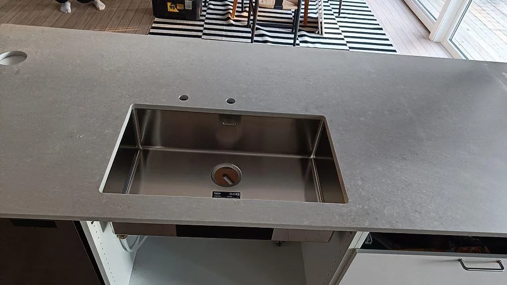 Detaljbild av underlimmad rostfri diskho i grå matt Caesarstone Clamshell köksbänkskiva med borrade hål på Torsö.