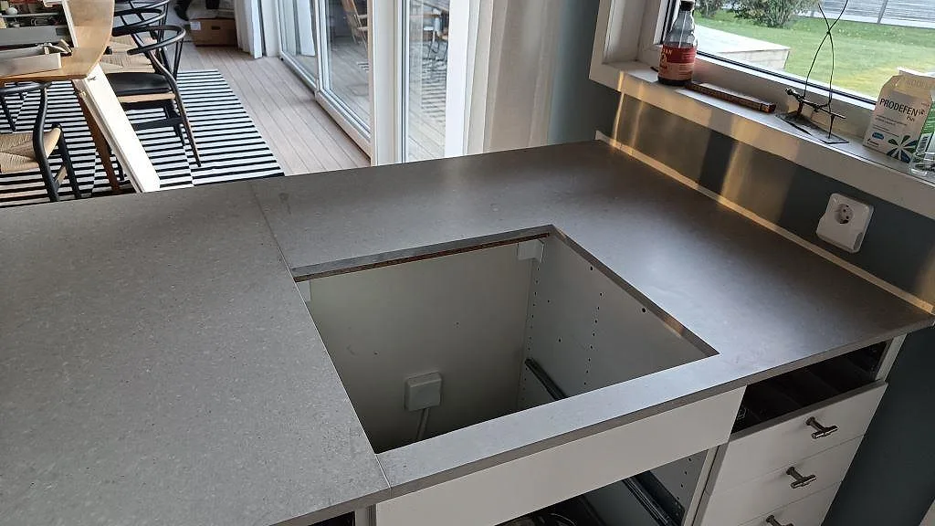 Köksbänkskiva i grå matt Caesarstone Clamshell med öppning för häll och bakkant mot fönster i kök på Torsö.