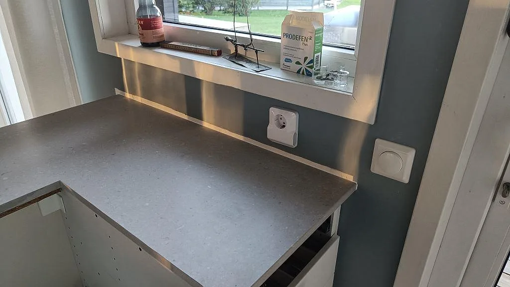 Detalj av matt Caesarstone Clamshell bänkskiva vid fönster och vägguttag i ett kök under montering på Torsö.