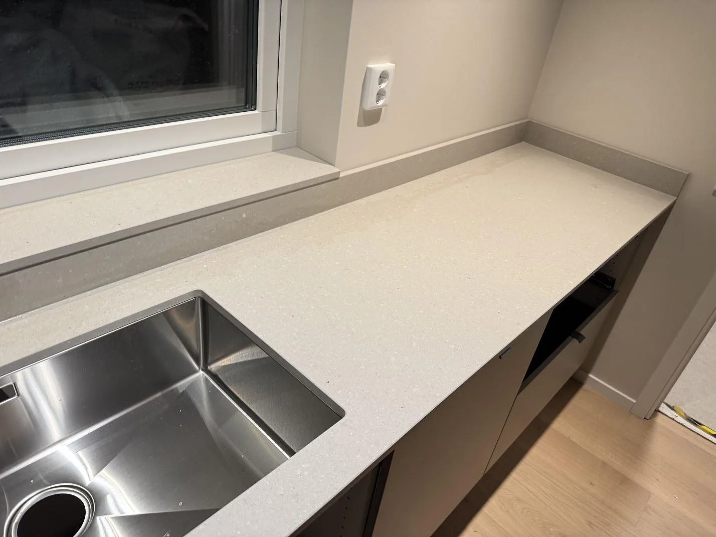 Köksbänkskiva i varm off-white Caesarstone Clamshell, matt kvartskomposit, med underlimmad rostfri diskho och fönsterbänk i samma sten i ett kök i Trelleborg.