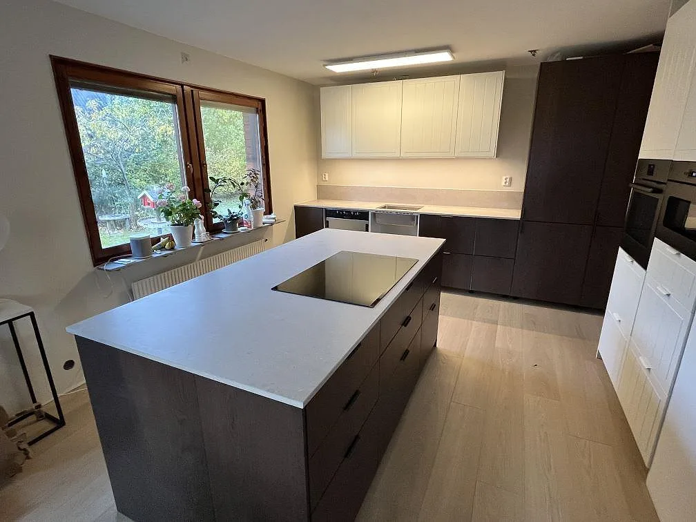 Matt köksbänkskiva i ljusgrå Caesarstone Clamshell komposit med integrerad induktionshäll i en stor köksö i Uppsala.