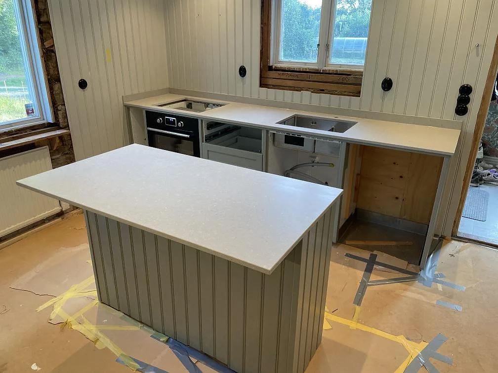 Köksö och köksbänkskiva i matt Caesarstone Clamshell kvartskomposit, med synlig diskho och hällöppning under montering i Uppsala.