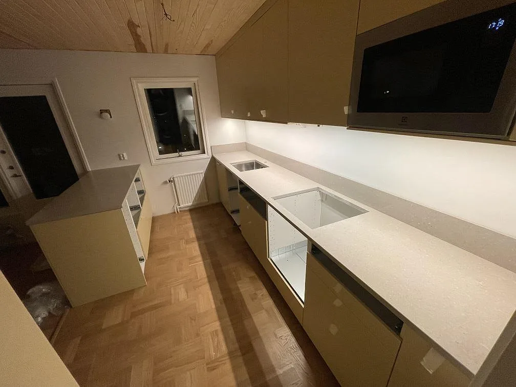 Polerad köksbänkskiva i Caesarstone Clamshell, ljus kvartskomposit, med låg stänkkant och urtag i ett kök i Vällingby.
