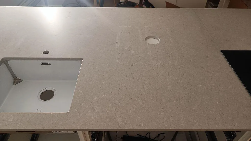 Detalj av matt Caesarstone Clamshell-bänkskiva med kabelgenomföring och svart häll i ett kök i Västra Frölunda.