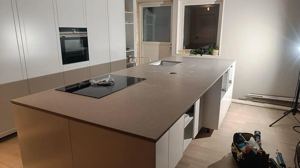 Stor köksbänkskiva i Caesarstone Clamshell, 20 mm matt komposit, med svart häll och diskho i ett kök i Västra Frölunda.