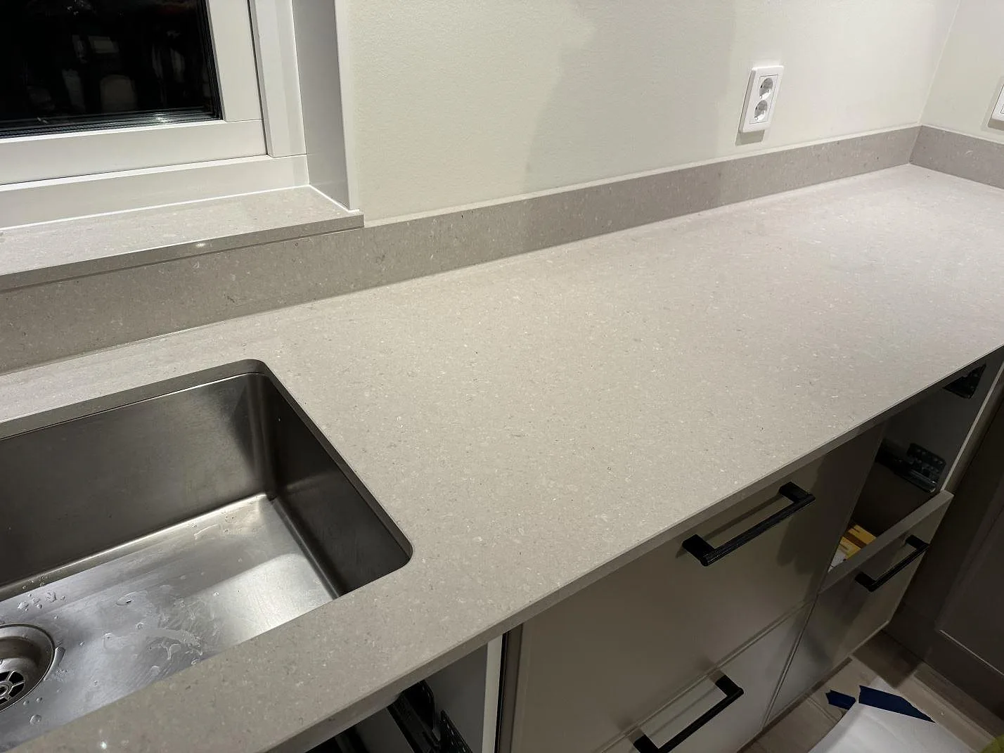 Köksbänkskiva i polerad Caesarstone Clamshell, 20 mm kvartskomposit, med underlimmad rostfri diskho och låg stänkkant i Veinge.