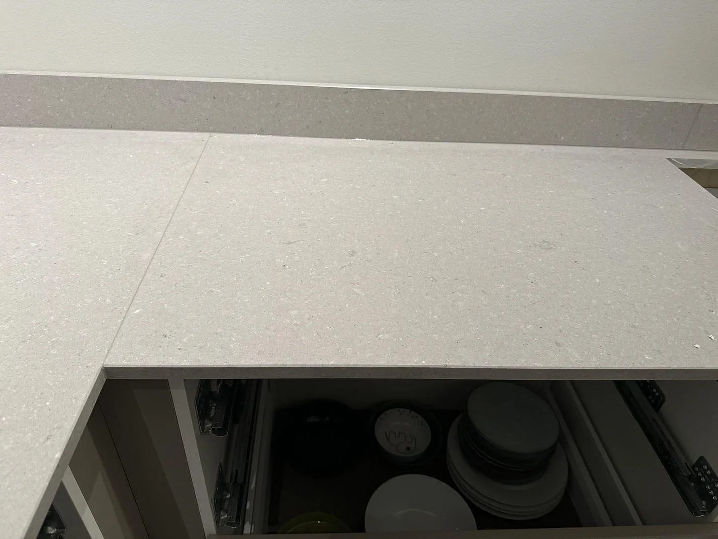 Rak del av köksbänkskiva i polerad Caesarstone Clamshell med ljus komposityta och öppen låda under montering i Veinge.