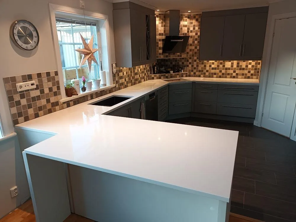 Köksbänkskiva i vit Caesarstone Frosty Carrina med mjuk grå ådring, polerad, i ett U-format kök med grå luckor, underlimmad diskho och infälld häll i Östhammar.