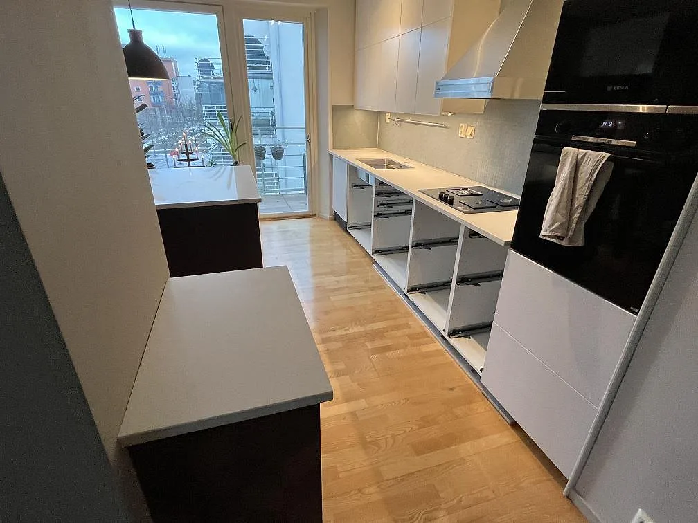 Polerad köksbänkskiva i vit Caesarstone Frosty Carrina med raka bänkrader, fönsterbänk och ljusa skåpstommar i Stockholm.