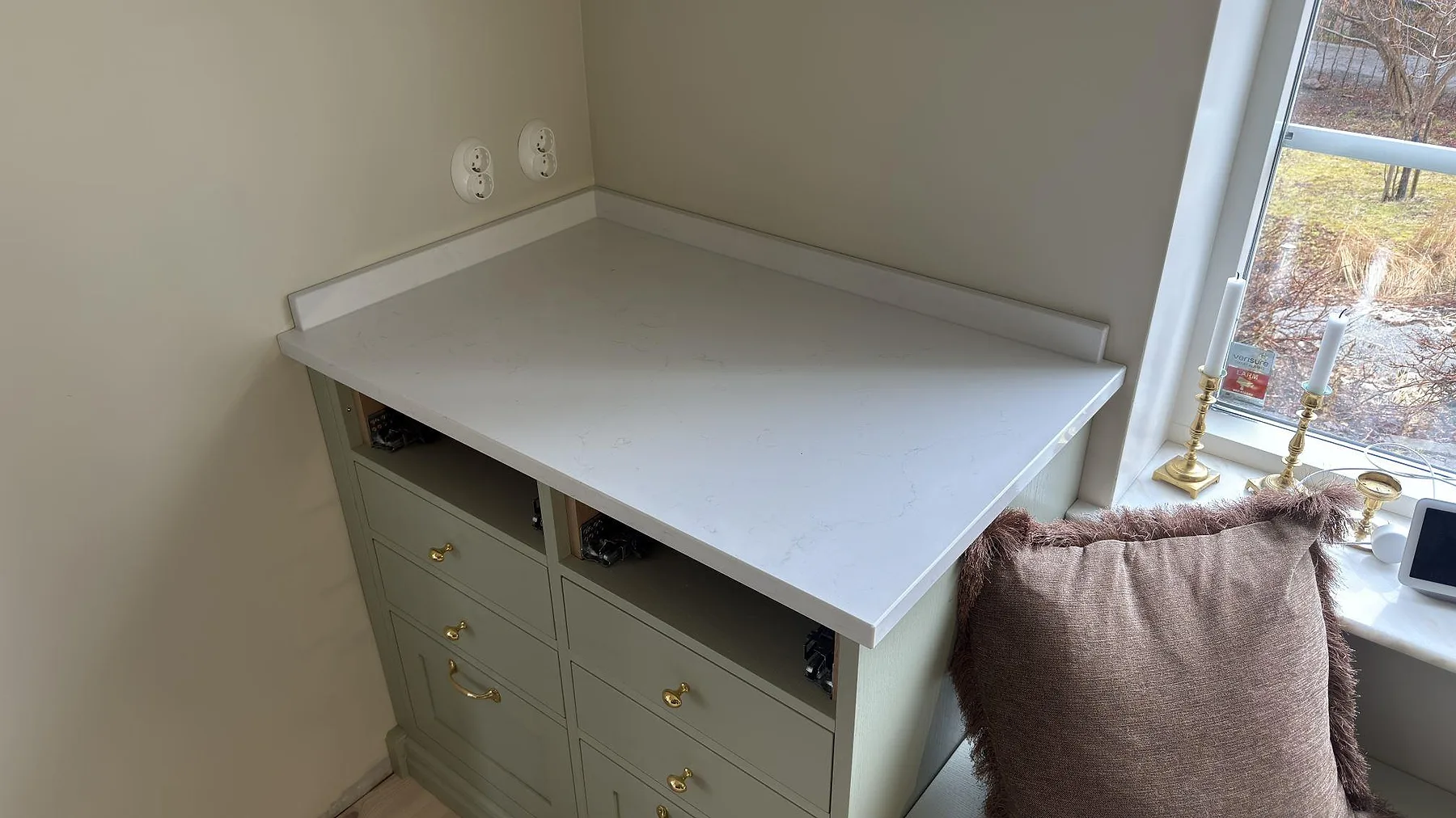 Polerad bänkskiva i Caesarstone Frosty Carrina med uppvikt kant på en grön bänkskåpsmodul i Vaxholm.