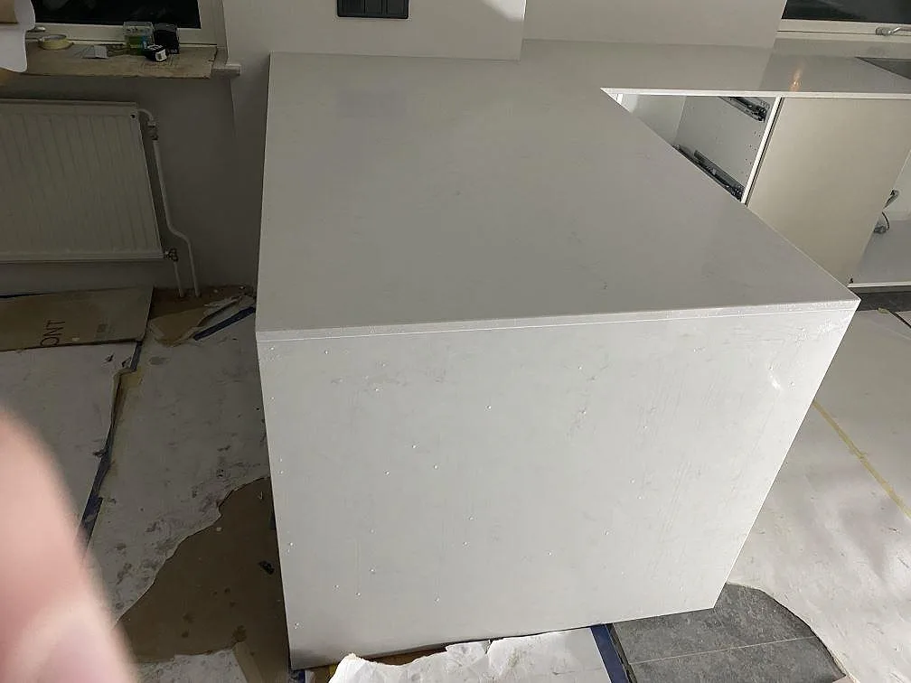 Bred köksyta i polerad Caesarstone London Grey-komposit med halvö och ljusa stommar under montering i Lund.
