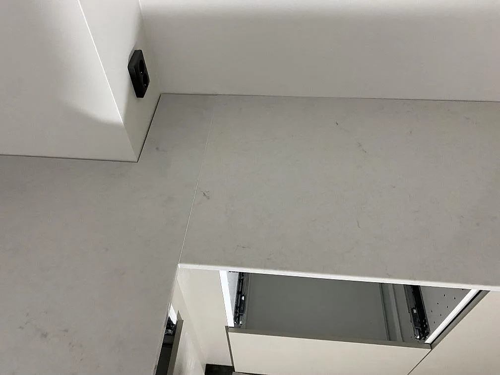 Hörndel av köksbänkskiva i polerad Caesarstone London Grey med skarv, grå ådring och vit köksinredning i Lund.