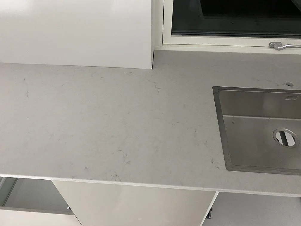 Polerad Caesarstone London Grey-komposit med rostfri diskho, ljus bänkyta och fönsterzon i ett kök i Lund.