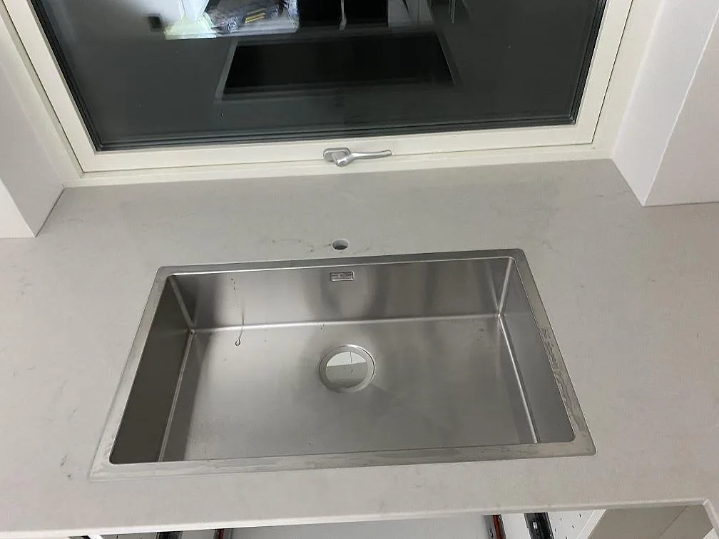 Köksbänkskiva i polerad Caesarstone London Grey med synlig rostfri diskho och blandarhål vid fönster i Lund.
