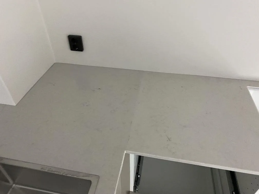 Närbild på polerad Caesarstone London Grey-bänkskiva med ljus grå ådring, väggzon och del av diskhon i Lund.