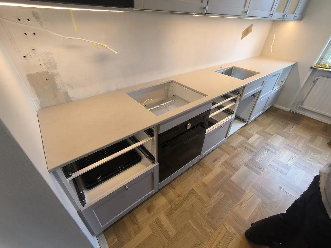 Polerad köksbänkskiva i Caesarstone London Grey i 20 mm kvartskomposit med diskho och uttag för spishäll i ett kök i Solna.