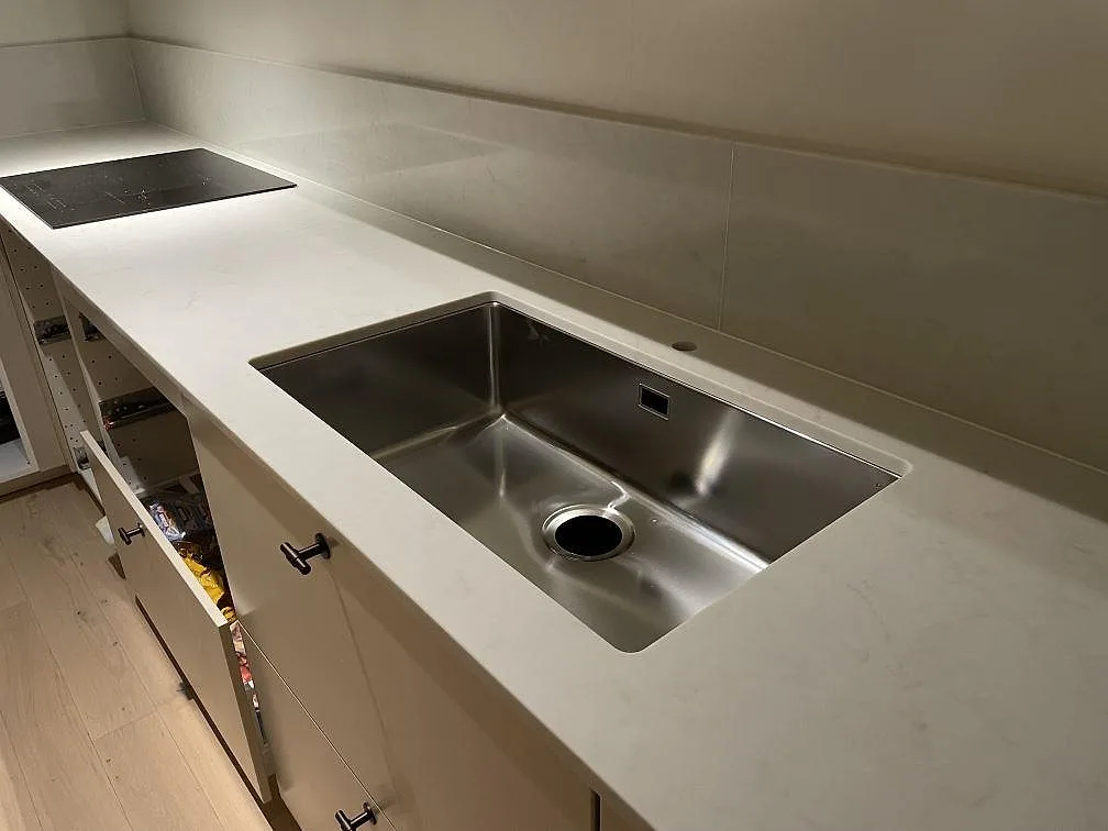 Underlimmad rostfri diskho och induktionshäll i en polerad köksbänkskiva av Caesarstone London Grey i ett kök i Vallentuna.
