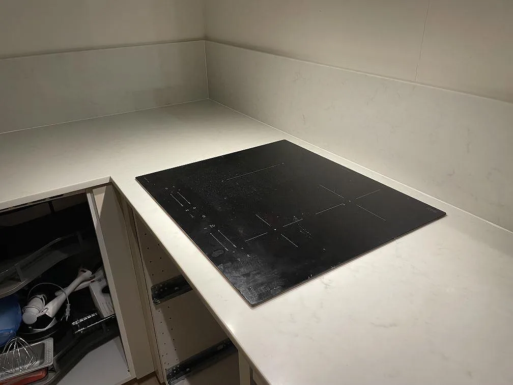 Infälld induktionshäll i en ljusgrå köksbänkskiva av Caesarstone London Grey med låg uppvikt stänkkant, kök i Vallentuna.