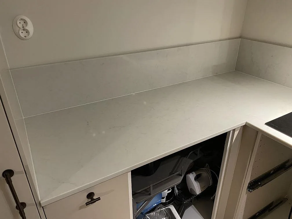 Ren bänkyta i polerad Caesarstone London Grey med låg uppvikt stänkkant i ett hörn av ett kök i Vallentuna.