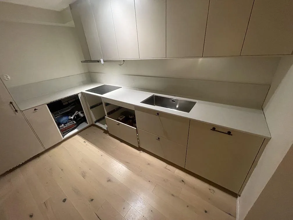 Köksbänkskiva i ljusgrå Caesarstone London Grey, polerad kvartskomposit, i ett L-format kök i Vallentuna med underlimmad rostfri diskho och infälld induktionshäll.