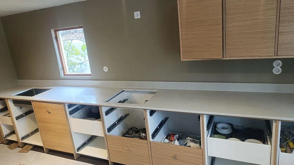 Köksbänkskiva i Caesarstone London Grey, polerad grå kvartskomposit, monterad längs hela köksväggen i ett kök under montering i Varberg.