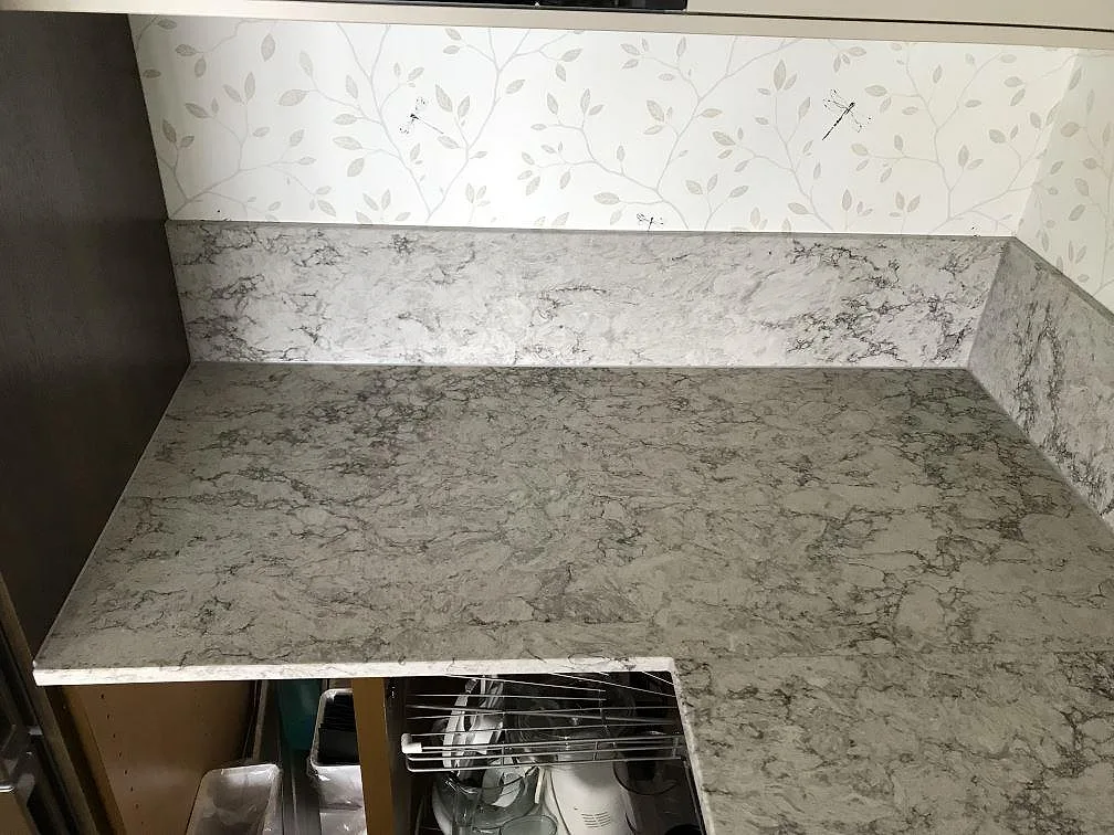 Hörnsektion av köksbänkskiva i Caesarstone Moorland Fog med uppvikt stänkkant och grå ådring i ett kök i Bohus.