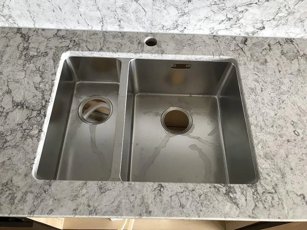 Underlimmad rostfri diskho med två bunkar i en köksbänkskiva av Caesarstone Moorland Fog kvartskomposit i Bohus.
