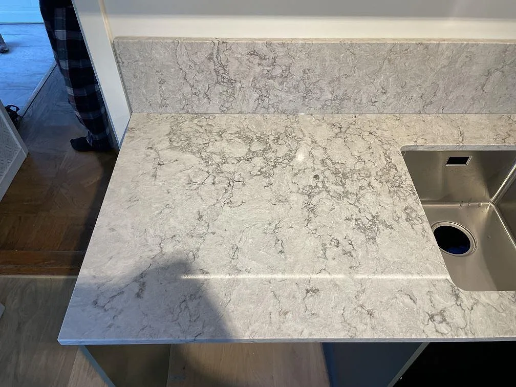 Ytdetalj av polerad Caesarstone Moorland Fog köksbänkskiva med grå ådring, stänkskydd och rostfri diskho i Borensberg.