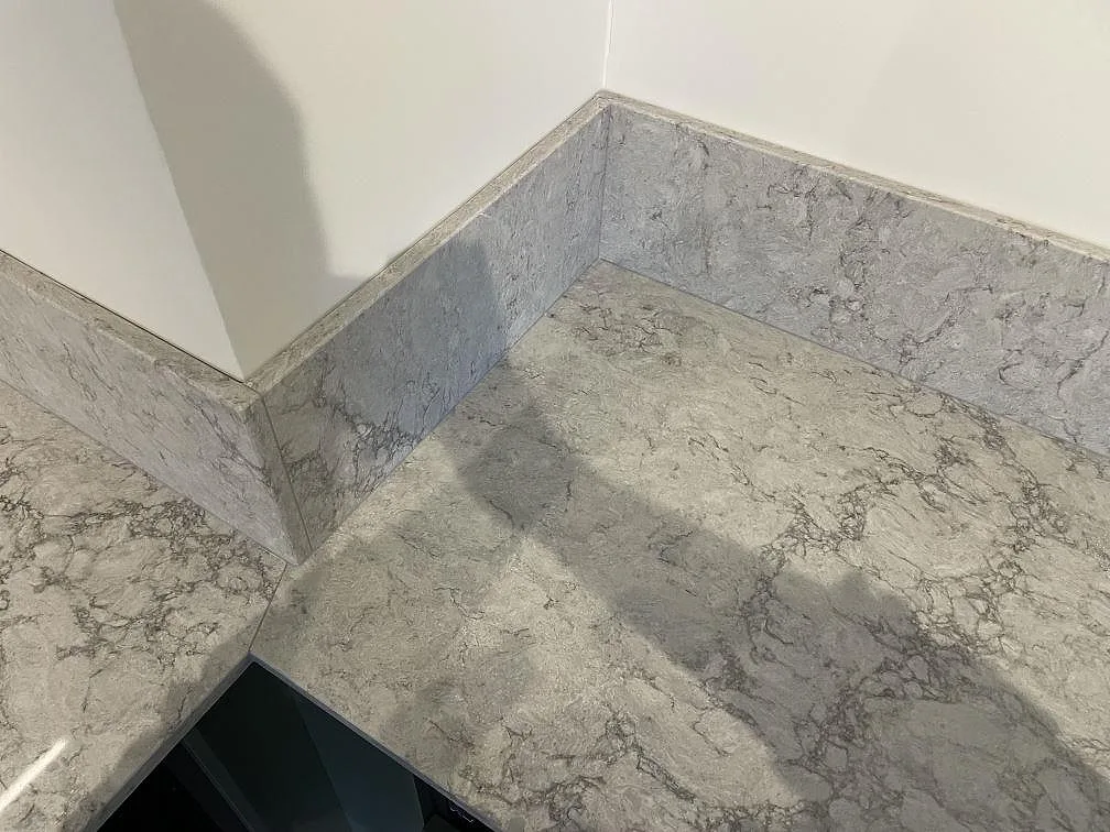 Närbild på hörn och uppvikt stänkskydd i polerad Caesarstone Moorland Fog med grå ådring i kök i Borensberg.