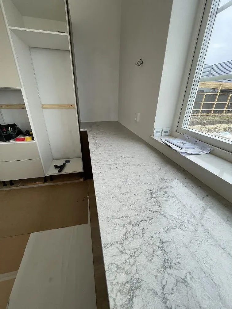 Väggbänk i Caesarstone Moorland Fog, polerad ljusgrå kvartskomposit med grå ådring, under fönstret i ett kök i Bunkeflostrand.